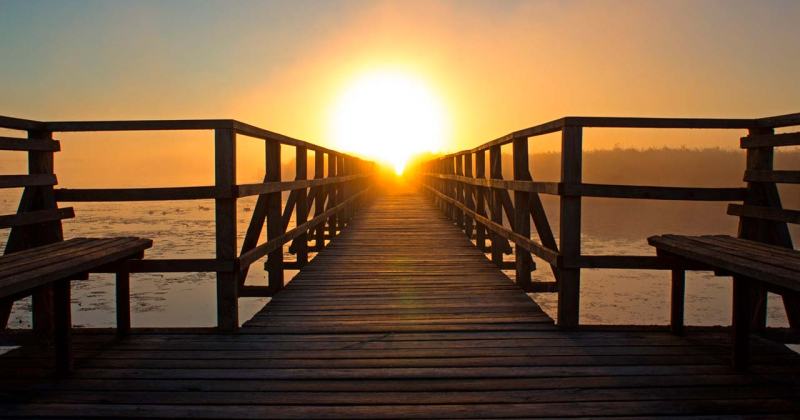 Un pont de fusta que va cap a l'horitzó, en direcció al sol naixent.